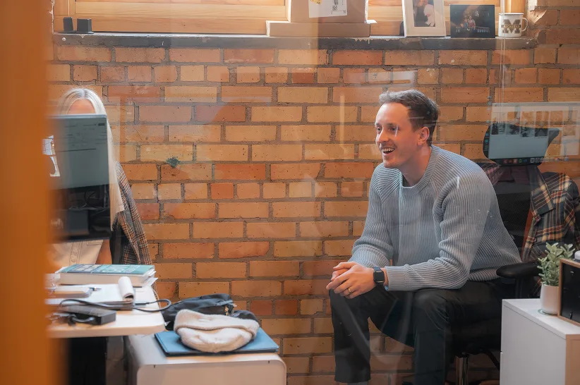 An AdShark team member laughing at his desk against the office brick wall