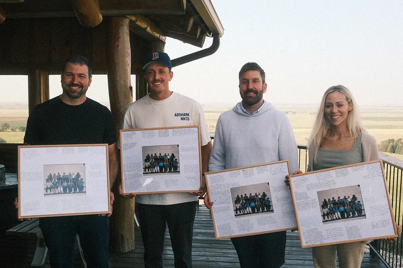 Four AdShark team members on a deck holding framed team photos