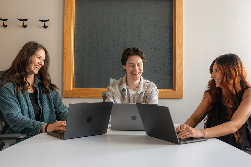 Three AdShark team members working together at a table of laptops